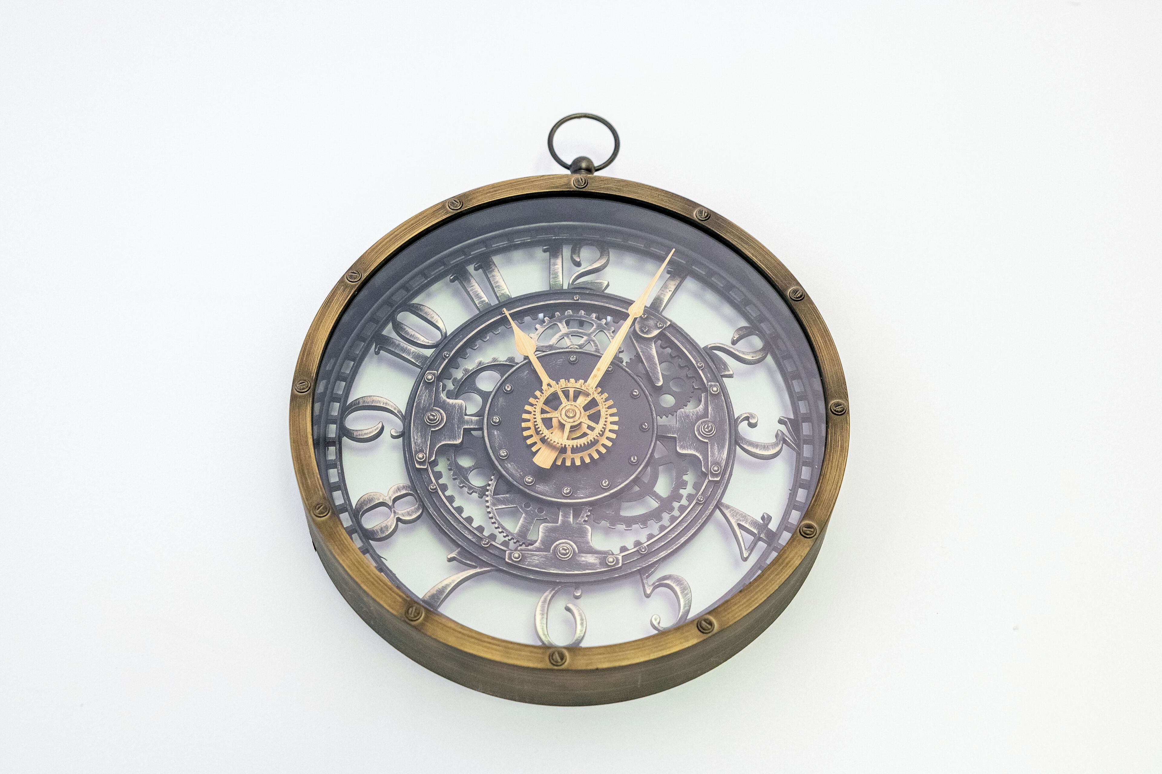 A wall-mounted clock with a mechanical design, featuring gears and a central wheel, mounted on a circular frame.