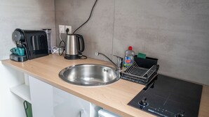 A kitchen with a stainless steel sink, a coffee maker, a kettle, a dish rack, and a built-in stovetop. - Charming, light-filled studio - Centre-ville-Gare (Cambrai)