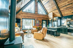 Amplia sala de estar con un ventanal grande, chimenea, sofá de cuero y una cocina con electrodomésticos modernos.