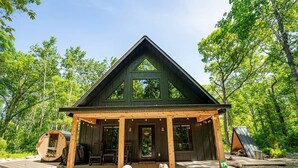 A wooden cabin with a porch, large windows, and a gravel area with stepping stones.