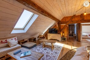 Ein gemütliches Dachzimmer mit Holzbalken, einer Couch, einem Fernseher und einem Esstisch.