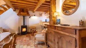 Una habitació acollidora amb un sostre de fusta, una llar de foc, una taula de dinar amb caires, un armari de fusta i un mirall rodó a la paret.