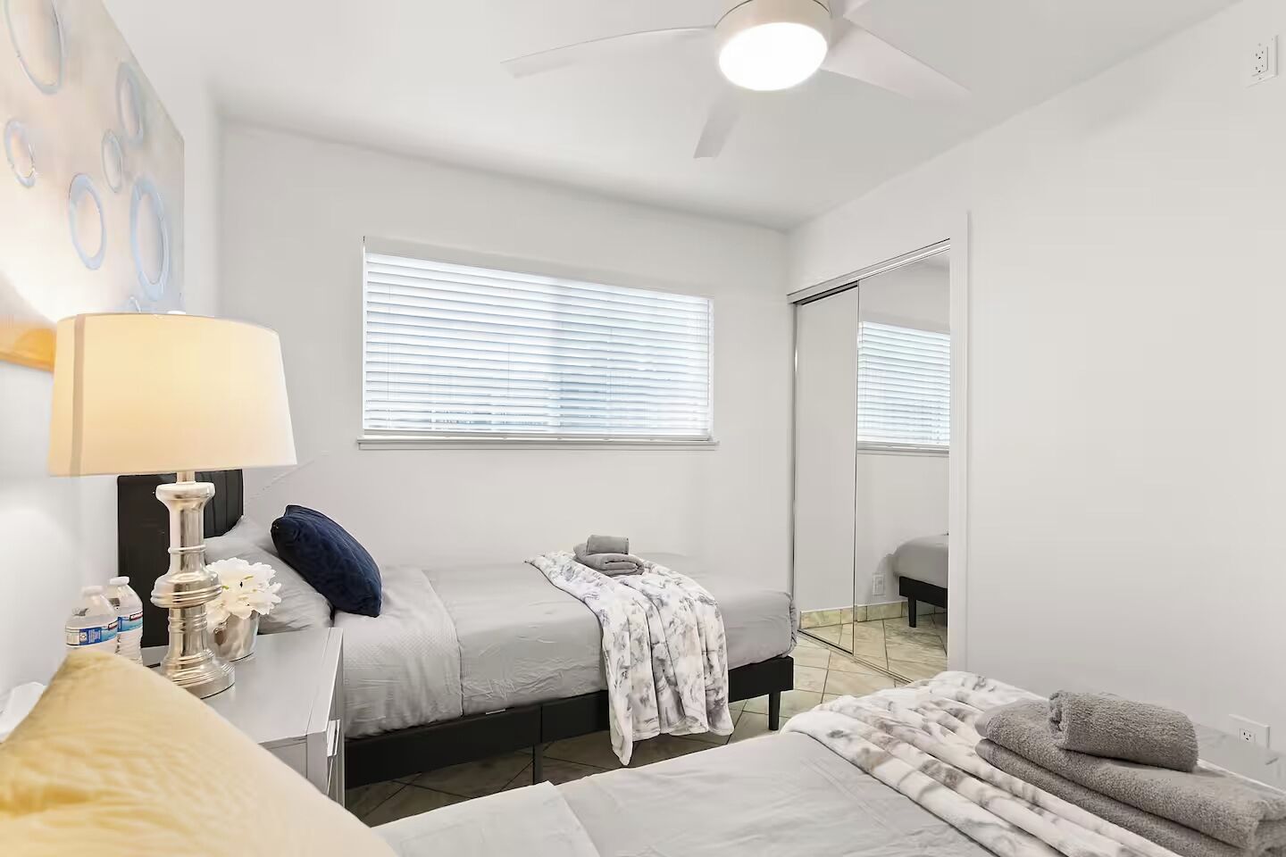 Quarto com cama, mesa de cabeceira, abajur e um espelho grande.