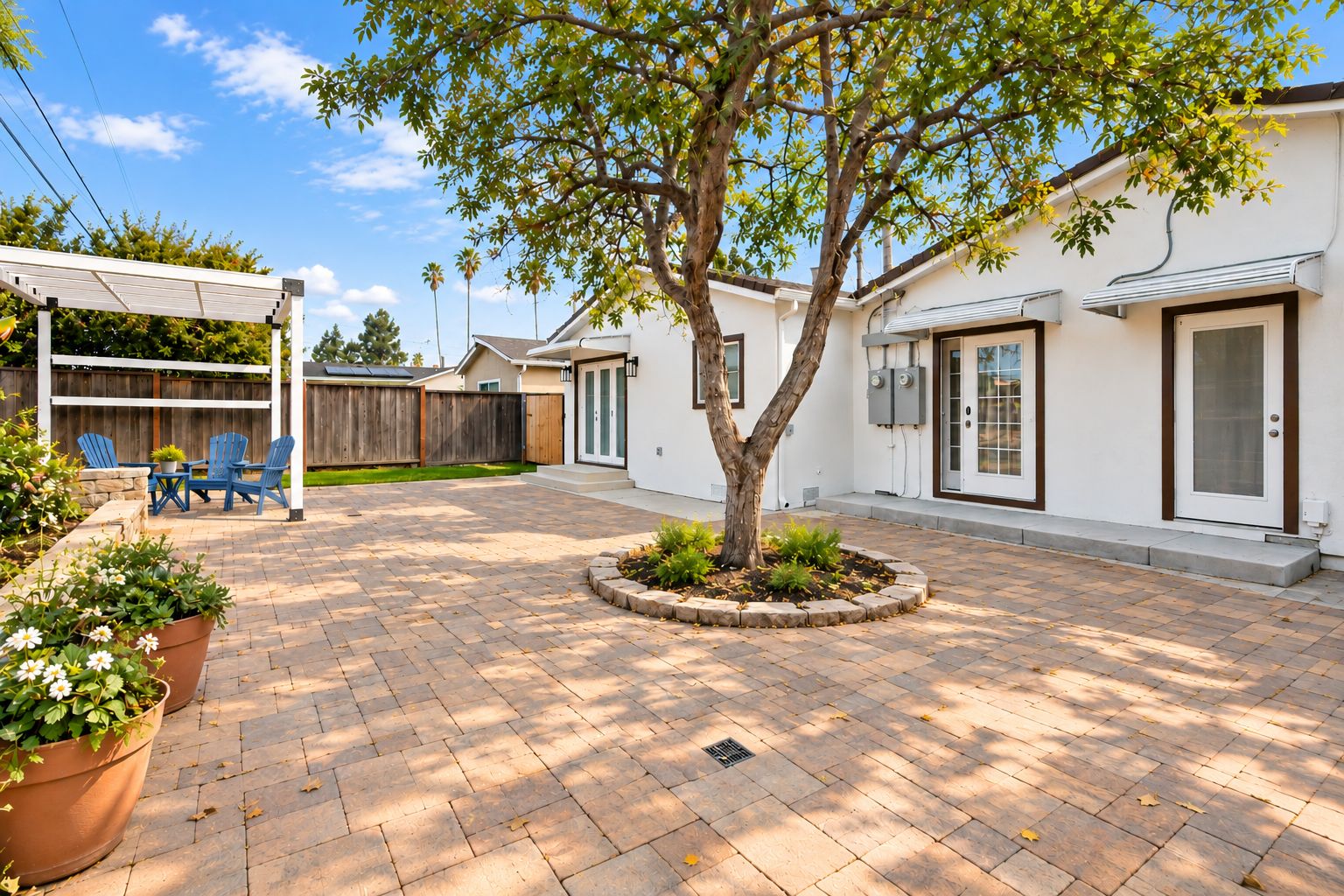A residential backyard with a paved patio, a wooden fence, and a tree.