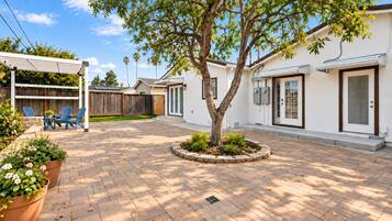 A residential backyard with a paved patio, a wooden fence, and a tree.