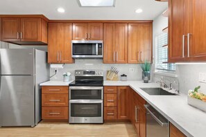 A modern kitchen with wooden cabinets, stainless steel appliances, and a skylight. - 3BR Home Ideal for Work Trips, Family & Long Stays (Fremont)