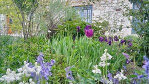 A stone building with a garden in front, featuring various flowers and greenery. - Une Maison Pour Deux (BILLIEME)