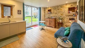 A modern kitchen with a large window, a dining area with a blue sofa, and a stone wall with built-in shelves. - Une Maison Pour Deux (BILLIEME)