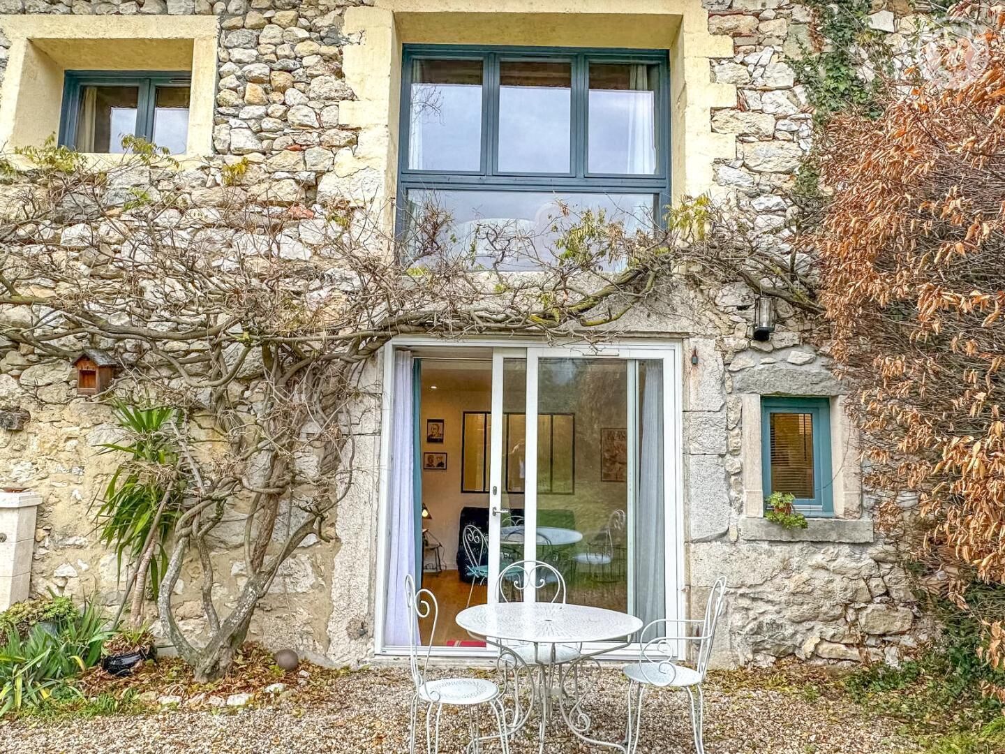 Ein Gebäude aus Stein mit Glastür, eine kleine Terrasse mit Tisch und Stühlen und Blick ins Innere.