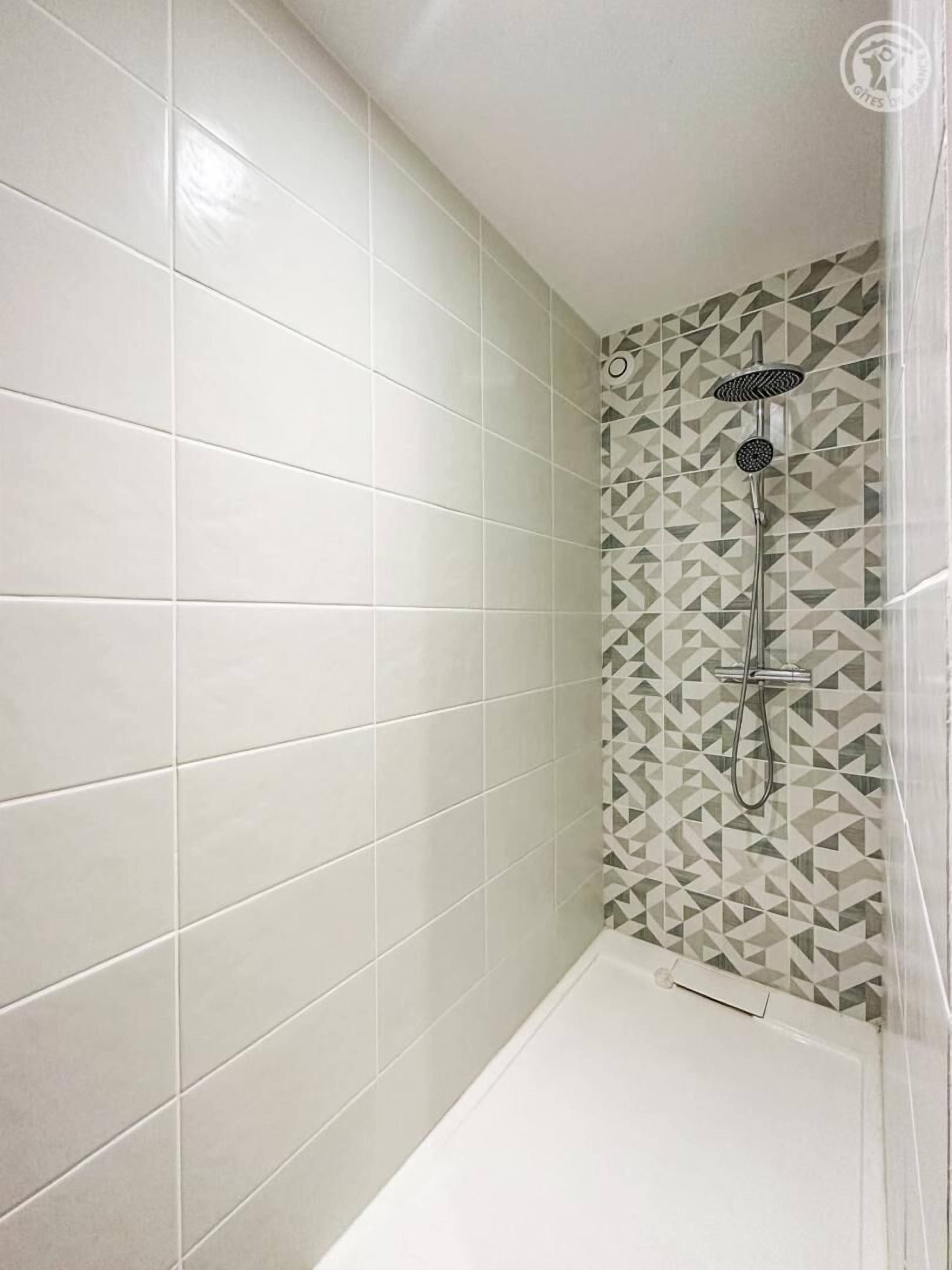 Ein Badezimmer mit weißen Fliesen, einer Dusche mit geometrischem Muster und einer weißen Badewanne.