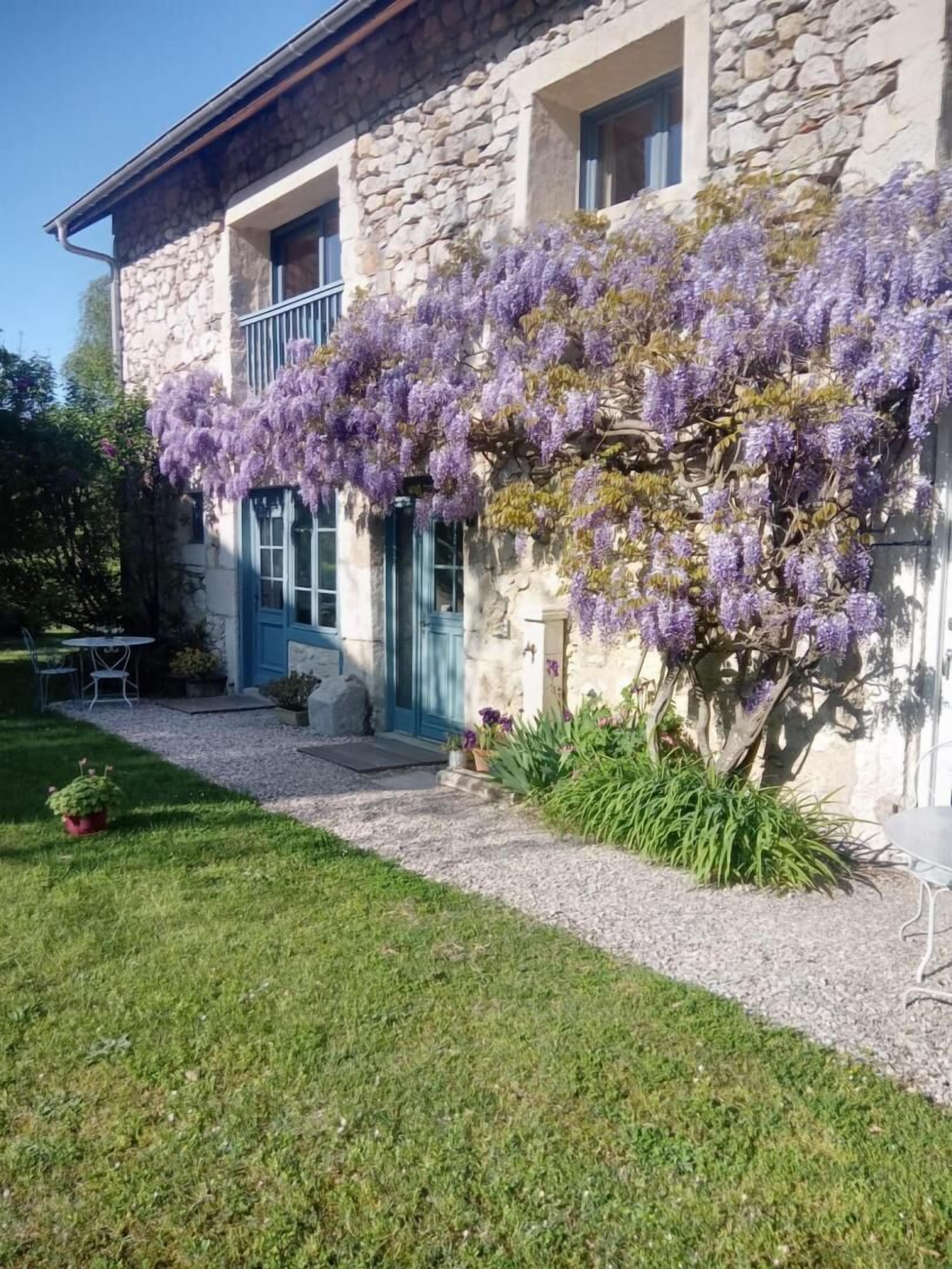 A stone building with a blue door, a small garden with purple flowers, and a gravel pathway.