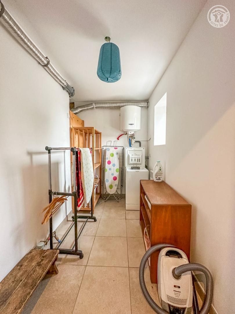 Un couloir étroit avec un banc en bois, un étendoir à linge, un aspirateur et un chauffe-eau.