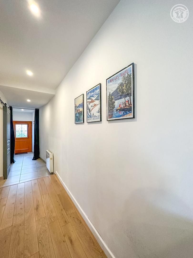 Een gang met houten vloer, witte wanden en drie ingelijste posters.