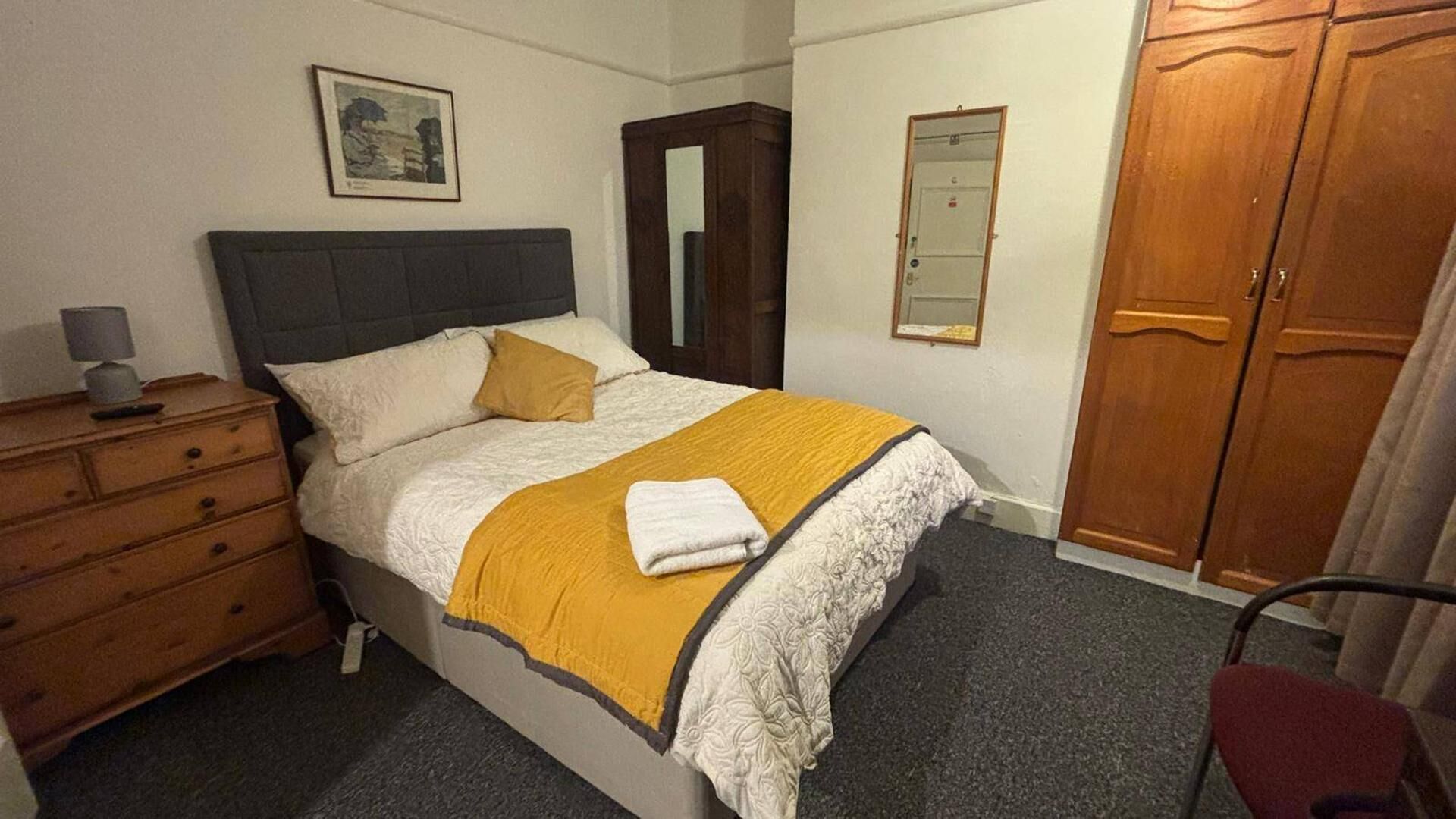 A bedroom with a bed, a dresser, a mirror, and a wardrobe.