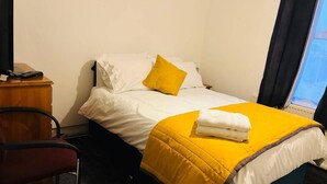 A hotel room with a bed, a chair, a desk, and a window.