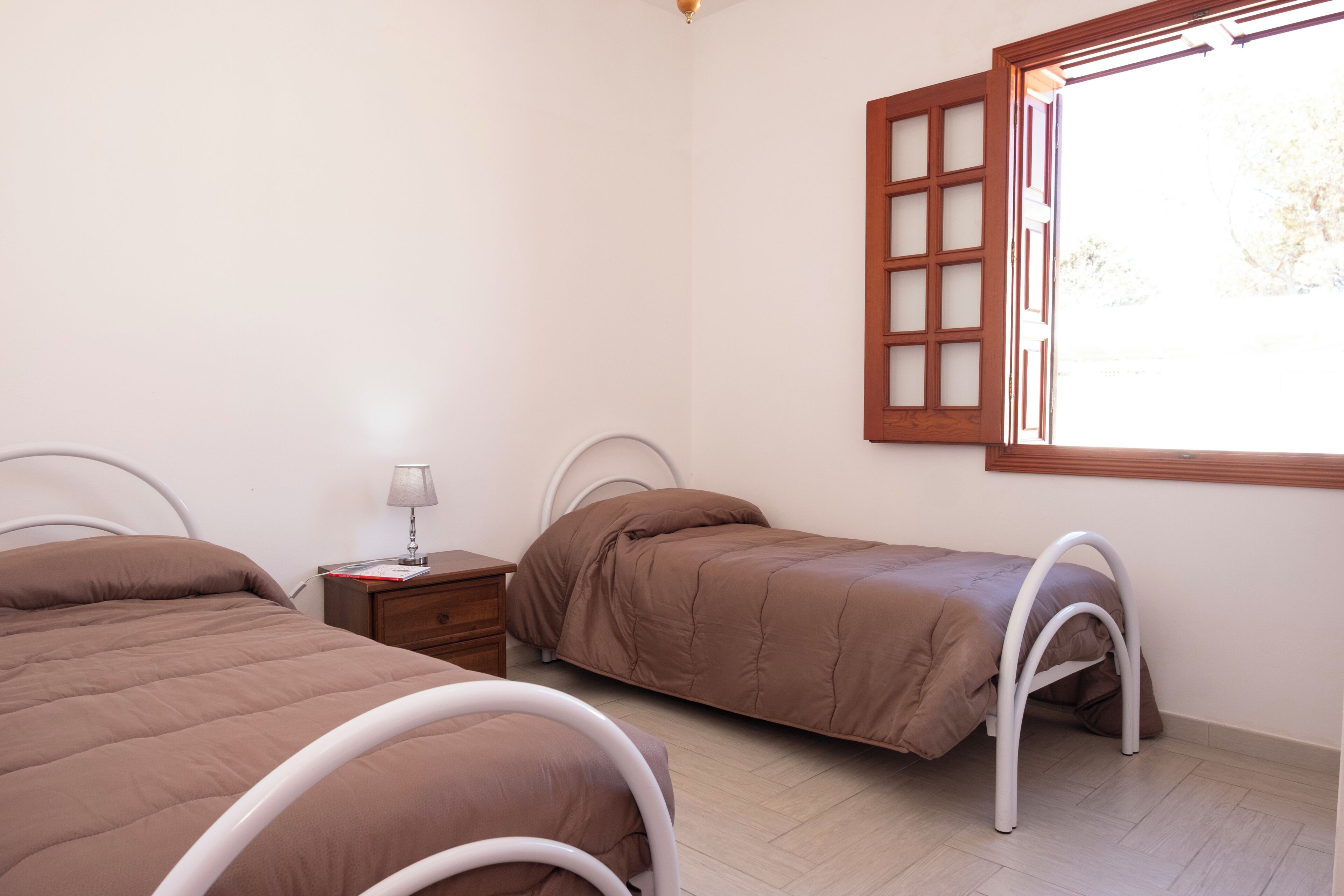 A bedroom with two beds, a nightstand, a lamp, and a window with a view.