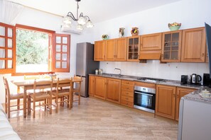 A kitchen with wooden cabinets, a dining table with chairs, a refrigerator, an oven, and a window with curtains. - Lucido House in front of the Tonnara (SAN VITO LO CAPO)