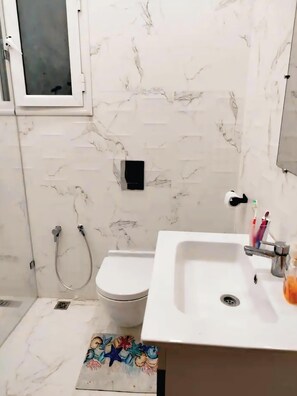 Une salle de bain avec un lavabo, des toilettes et une douche, le tout de couleur blanche.