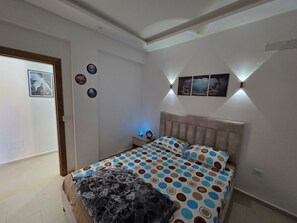 Une chambre à coucher comprenant un lit, une table de chevet, une lampe fixée au mur et une porte.