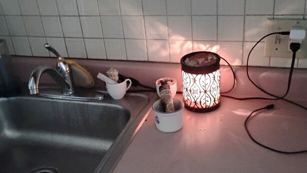 Una cocina con un lavamanos de acero inoxidable, una taza blanca y una vela encendida sobre la encimera.