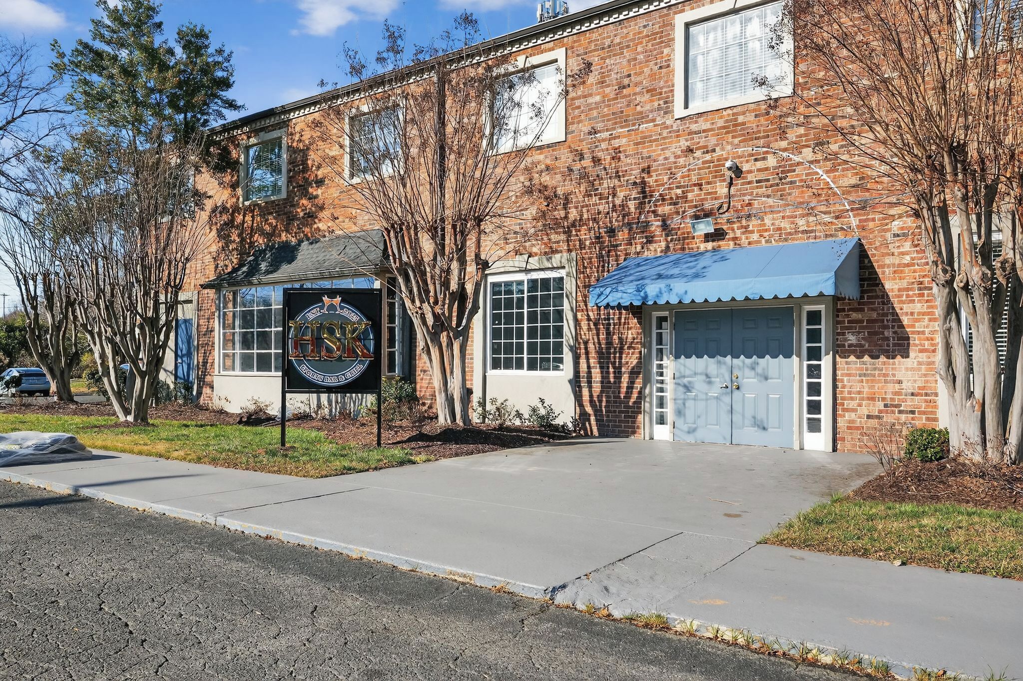 A brick building with a blue awning, a garage door, and a sign with a circular emblem.