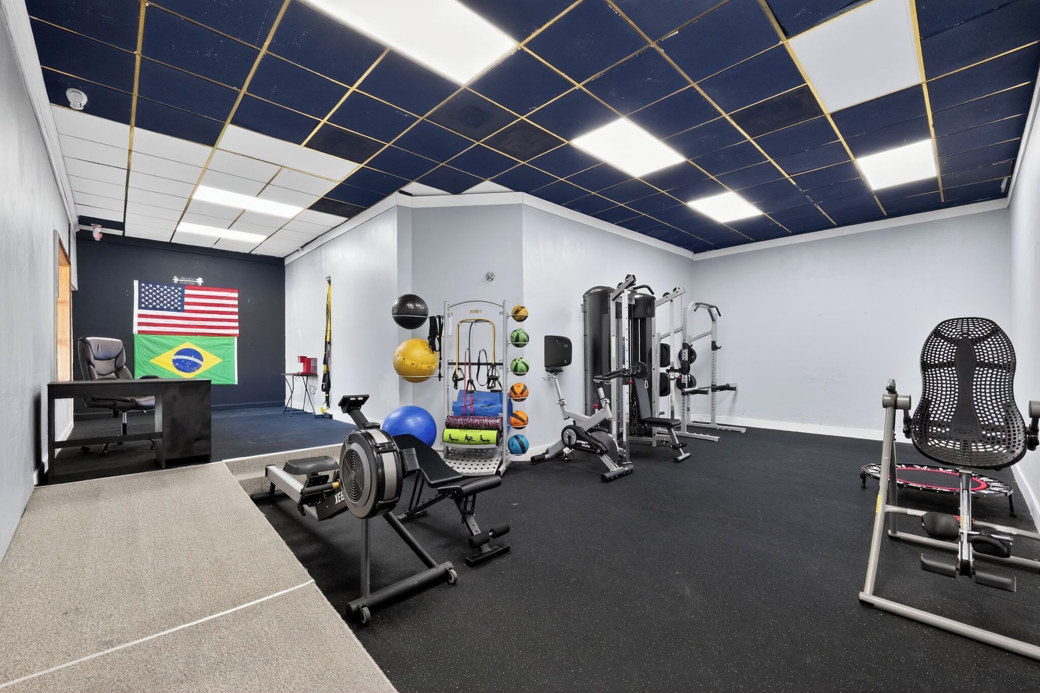 Une salle de sport équipée de matériel d’exercice, décorée de drapeaux et dotée d’un plafond orné d’un motif quadrillé.