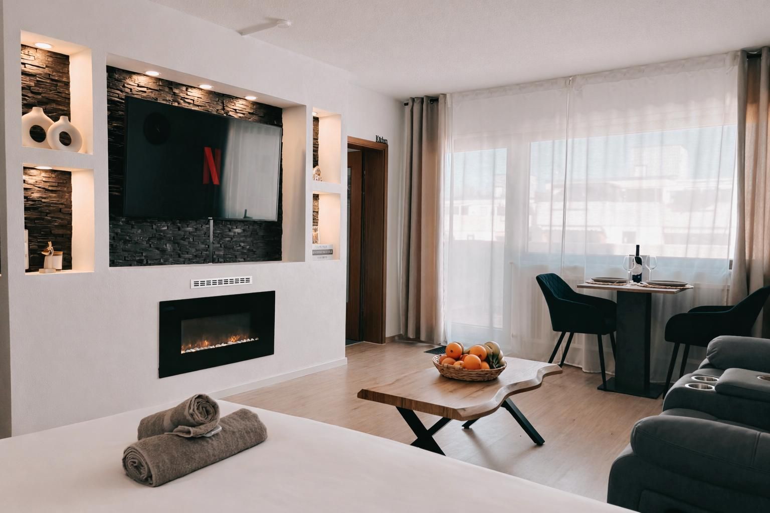 A modern living room with a fireplace, a dining area with a table set for two, and a seating area with a sofa.