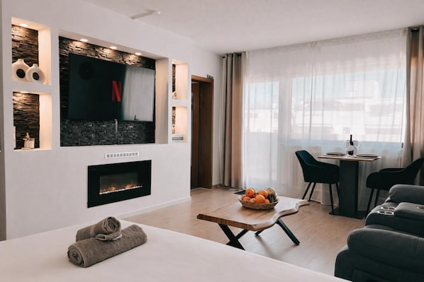 A modern living room with a fireplace, a dining area with a table set for two, and a seating area with a sofa.