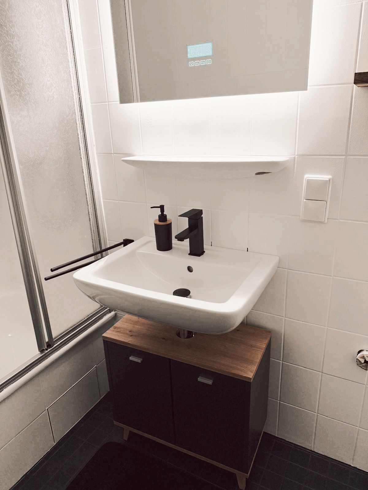 A bathroom with a white sink, black faucet, and a wooden cabinet below.
