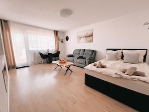 A modern bedroom with a bed, a sofa, a dining table with chairs, and a window with curtains.