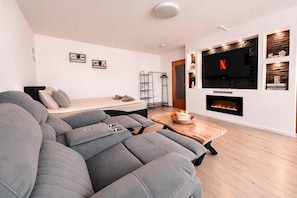 A modern living room with a grey sectional sofa, a wooden coffee table, a fireplace, and a mounted TV. - Vacation Apartment - Cozy Home by Li-Apartments (Pforzheim)