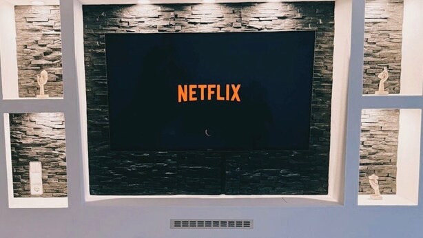 Moderni olohuone, jossa on suuri, seinälle asennettu litteänäyttöinen televisio, sen alla takka ja kivipaneelien päällä koriste-esineitä.