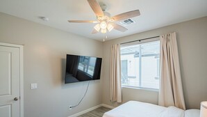 A bedroom with a ceiling fan, a TV mounted on the wall, a window with curtains, and a bed. - The One 216 (Glendale)