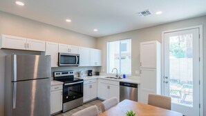A modern kitchen with stainless steel appliances, white cabinetry, and a dining area with a wooden table and chairs. - The One 216 (Glendale)