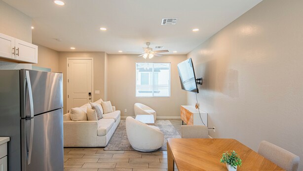 A modern kitchen with a stainless steel refrigerator, a wooden dining table with a potted plant, a white sofa, and a ceiling fan. - The One 216 (Glendale)