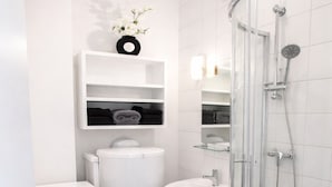Une petite salle de bain comprenant des toilettes, un lavabo et une douche fermée par une paroi de verre.