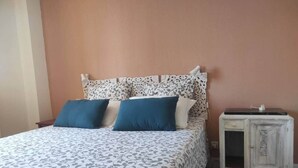 Une chambre à coucher avec une couvre-lit à motifs, deux oreillers, une table de chevet et une armoire.