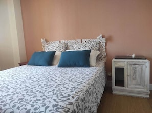 Un dormitorio con una colcha estampada, dos almohadas, una mesita de noche y un armario.