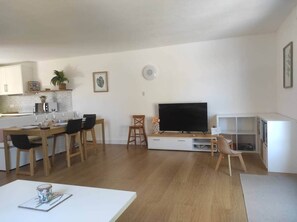 Een moderne woonkamer met een eethoek, een flatscreen televisie en een wit kastje.