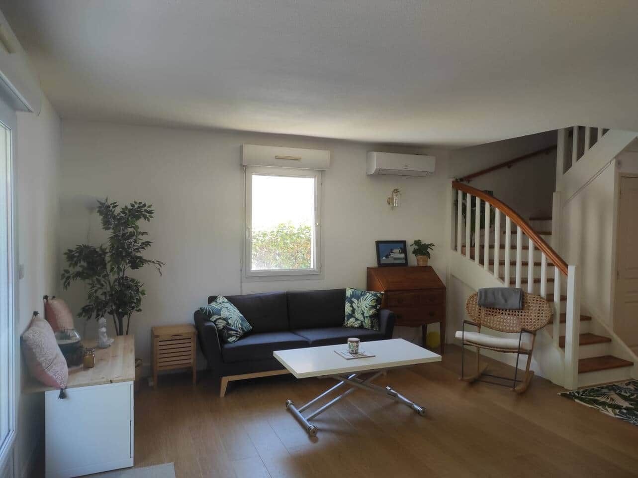 Un salon avec un canapé, une table basse, un plancher en bois, un escalier et une fenêtre.