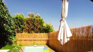 Un jardin avec une piscine, une terrasse en bois et un fauteuil suspendu.