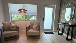 A modern living room with two sofas, a console table with a mirror, and a door leading outside. - Renovated 1 Bedroom, Boutique Mid-Century Building (Fort Lauderdale)