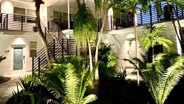 A multi-story building with a central staircase, surrounded by palm trees and lush greenery. - Renovated 1 Bedroom, Boutique Mid-Century Building (Fort Lauderdale)