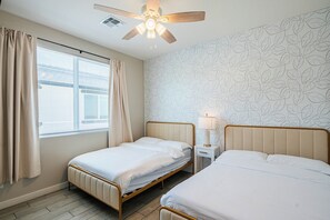 Ein Hotelzimmer mit zwei Betten, einem Deckenventilator, einem Fenster mit Vorhängen, einem Nachttisch mit Lampe und einer Wand mit Muster.