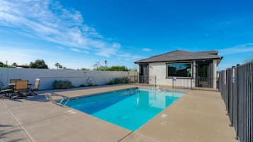 A swimming pool with a small building, a covered seating area, and a fenced patio.