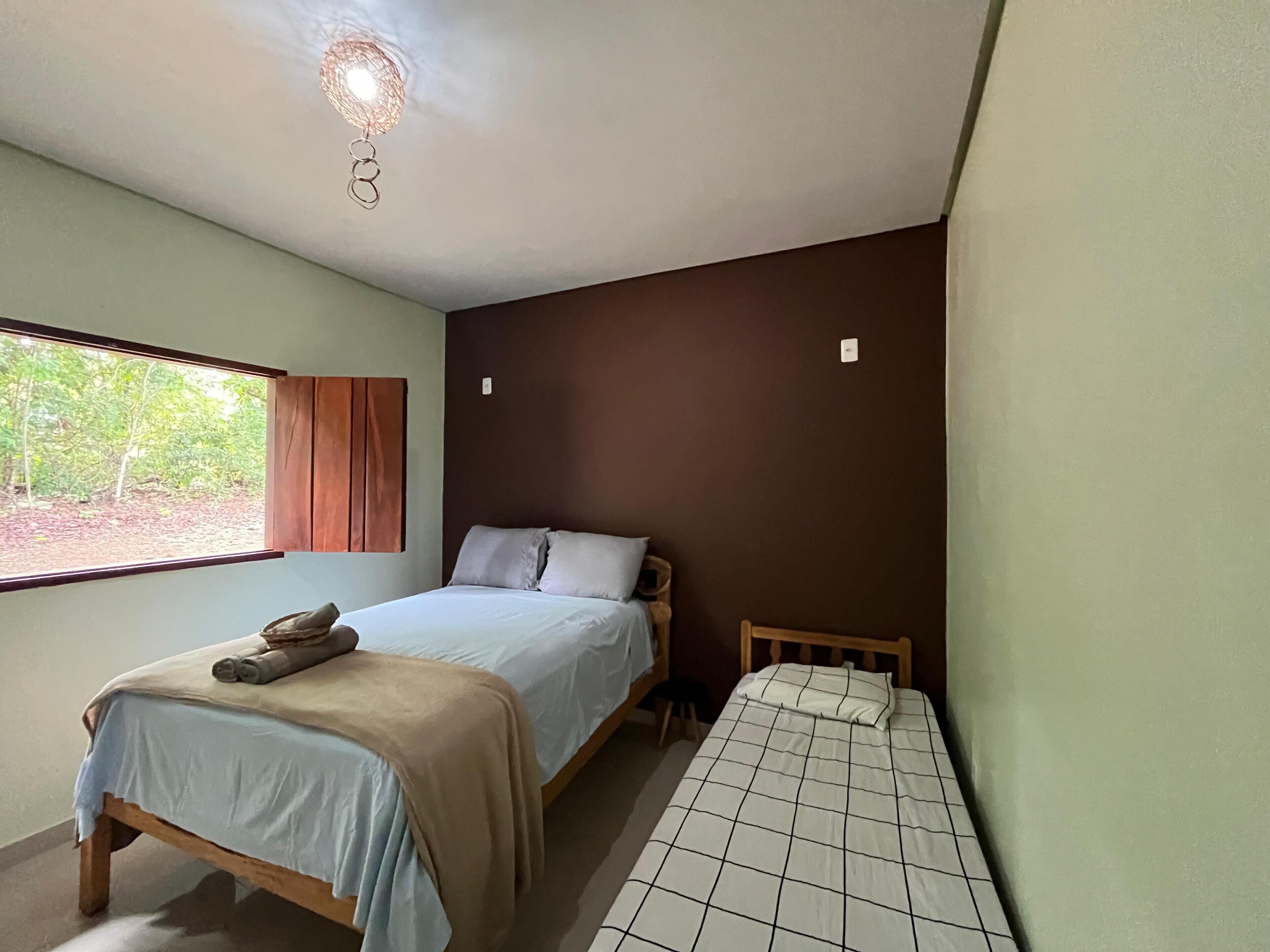 Een slaapkamer met een bed, een kinderbed, een raam met gordijnen en een plafondlamp.