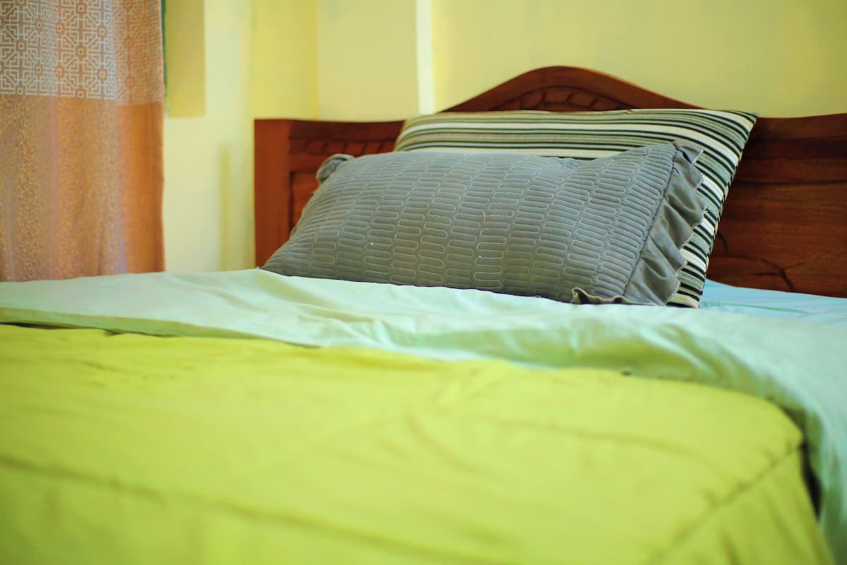 A bed with a wooden headboard, a green blanket, and two pillows.