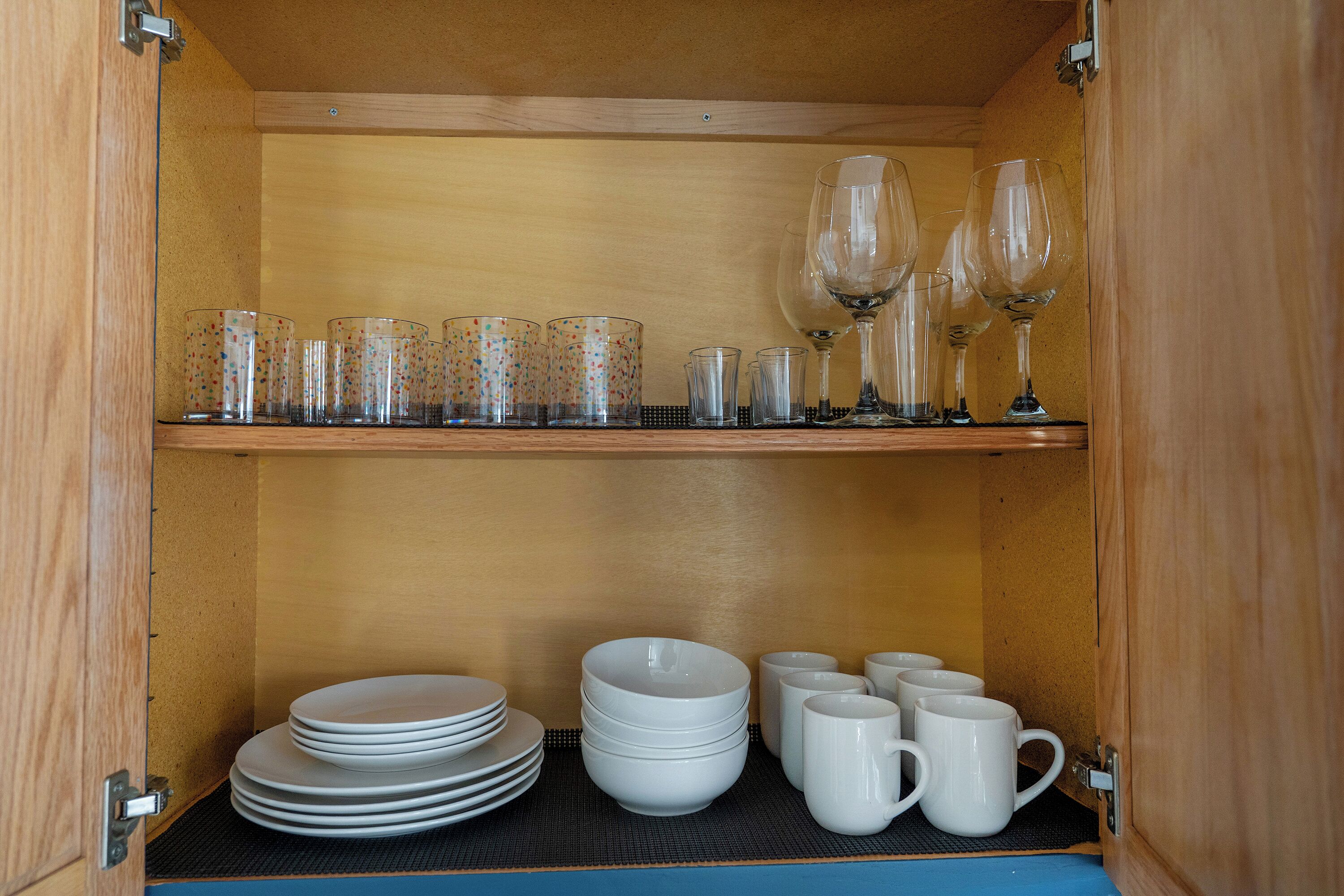 A wooden cabinet with shelves containing glassware and white ceramic dishes.