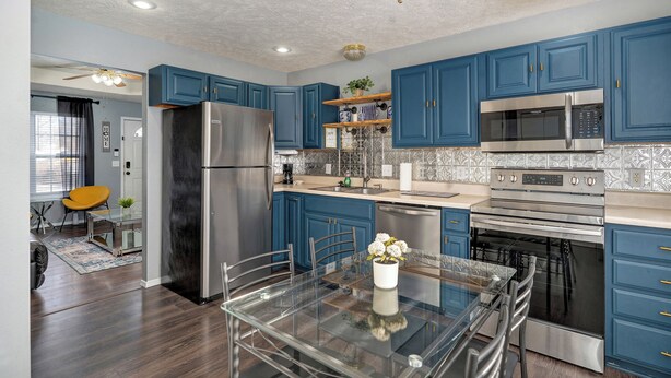 A modern kitchen with blue cabinets, stainless steel appliances, and a glass dining table. - Belmont Blue Stylish Retreat - Bass Pro+MSU+Downtown+Drury (Springfield)