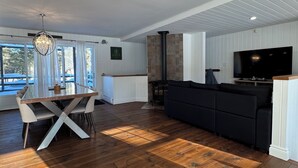 A spacious living area with a wooden floor, a dining table, a black sofa, and a TV.